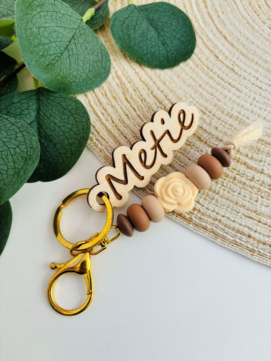 Handgemaakte sleutelhanger met siliconen kralen in bruin en beige tinten. Voorzien van een uit hout gelaserde naamplaatje.