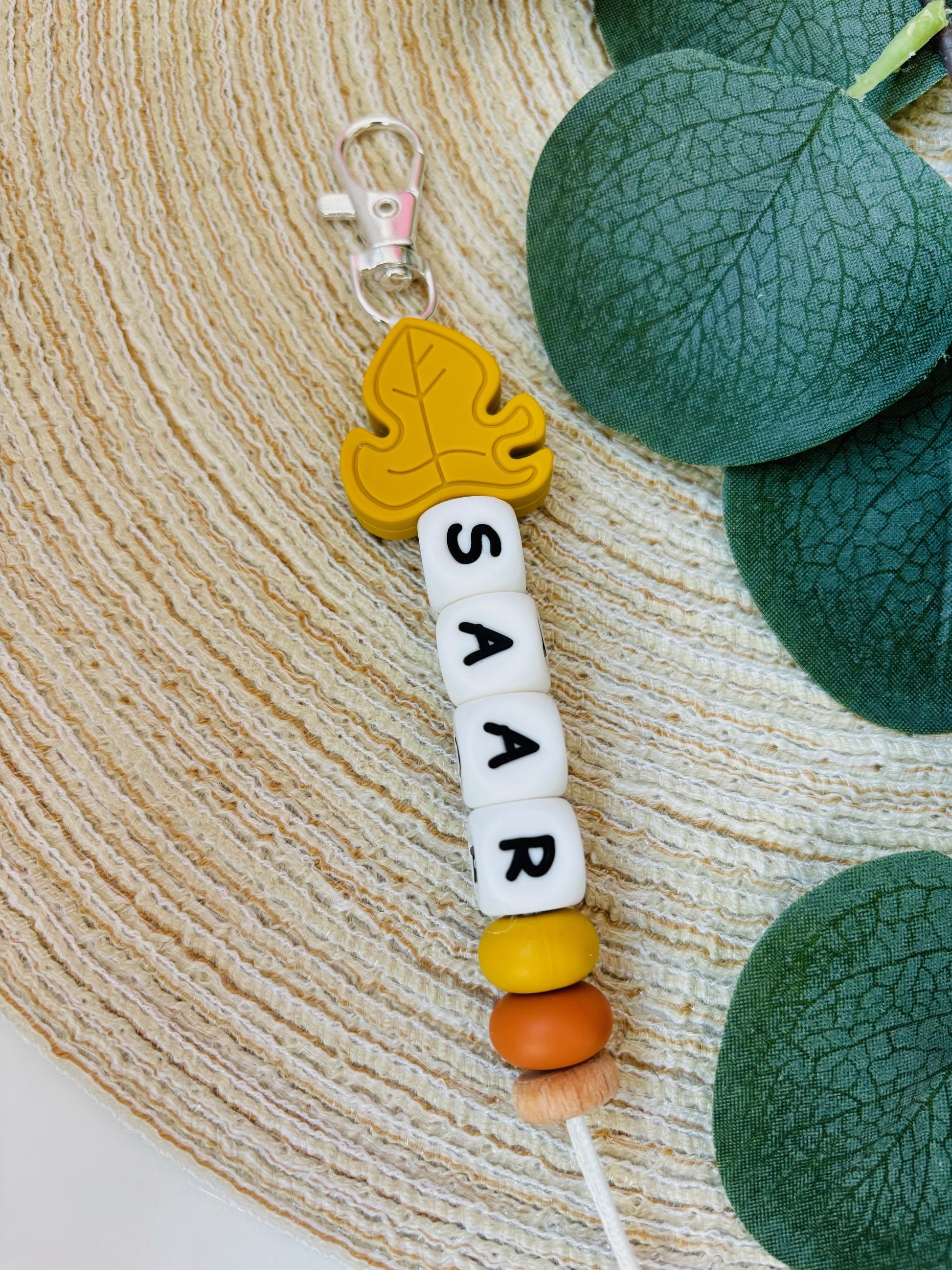 Handgemaakte sleutelhanger met naam naar keuze. Met een siliconen Monstera blad in mosterd kleur, naam in witte letters.