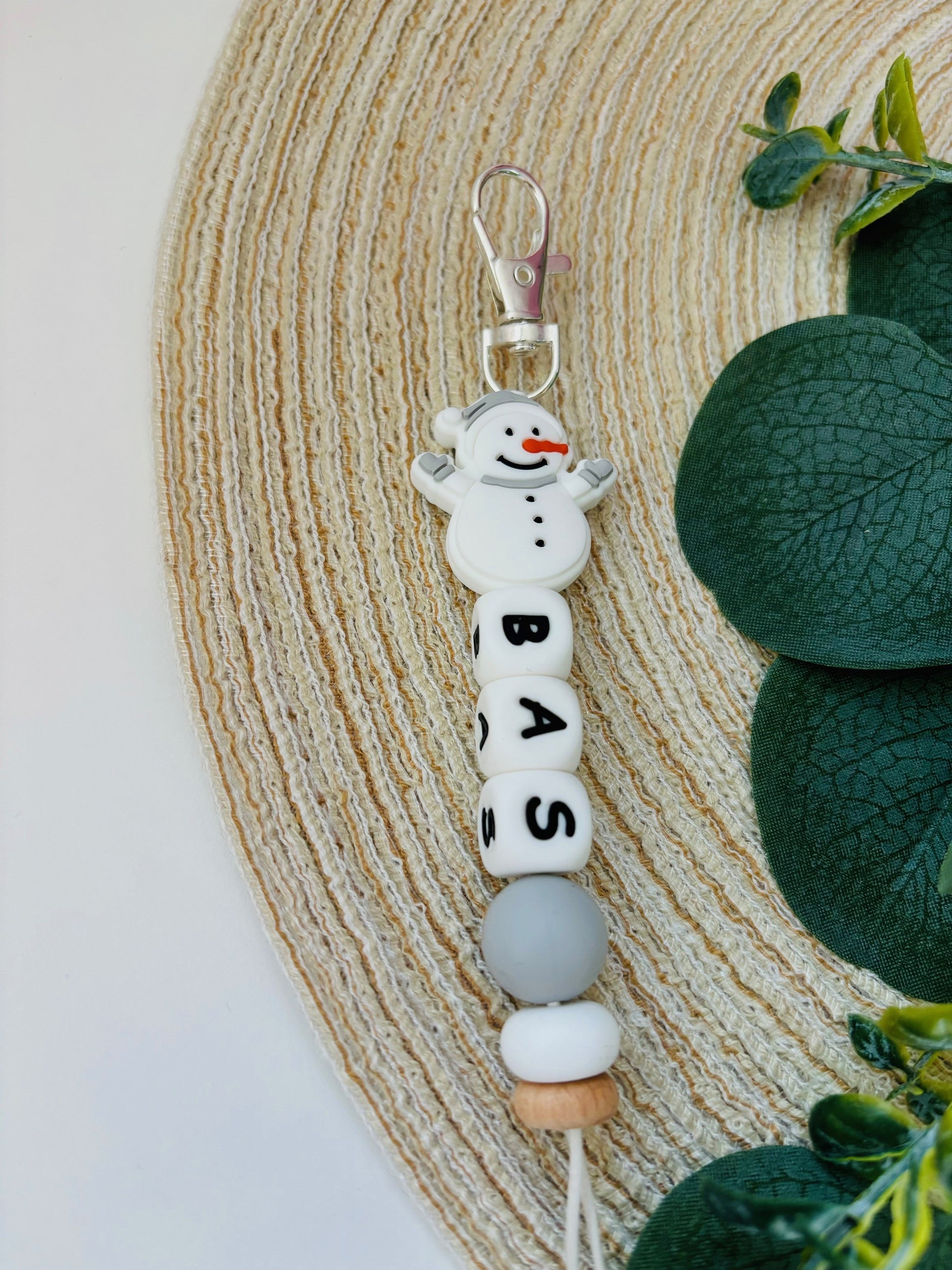 Handgemaakte sleutelhanger met naam naar keuze. Met een siliconen sneeuwpop in licht grijs en wit, naam in witte letters.